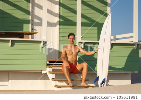 A man surfer sits with a board at a shore house 105611981