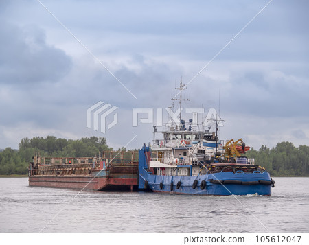 A river towboat pushing an old rusty barge down the river. Towboat and barge connected 105612047