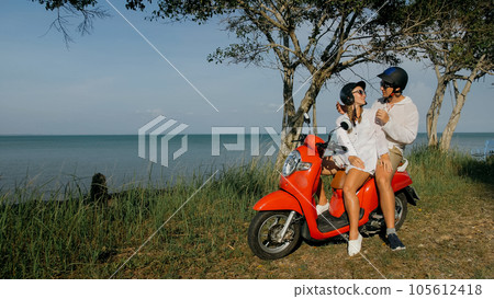 Scooter road trip. Love couple on red motorbike in white clothes on forest road trail. Just married woman and man kiss, hugs, sit on motorbike. Scooter road trip. Love couple on red motorbike in white clothes on forest road trail. Just married woman and man kiss, hugs, sit on motorbike. 105612418