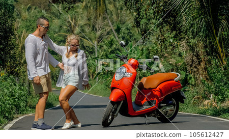 Love couple on red motorbike in white clothes, sunglasses on forest road trail trip. Dancing road. Two caucasian tourist woman man dance near scooter. 105612427