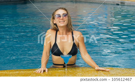 The wide middle shot pretty woman drinking blue cocktail alcohol liquor in swimming pool at hotel. Portrait of sexy girl in pool outdoor. 105612467