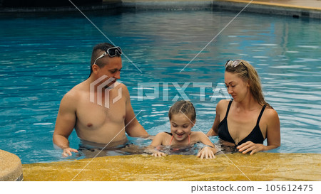 The mother and father with little daughter have fun in the pool. Mom and dad plays with the child. The family enjoy summer vacation in a swimming. The mother and father with little daughter have fun in the pool. Mom and dad plays with the child. The family enjoy summer vacation in a swimming. 105612475