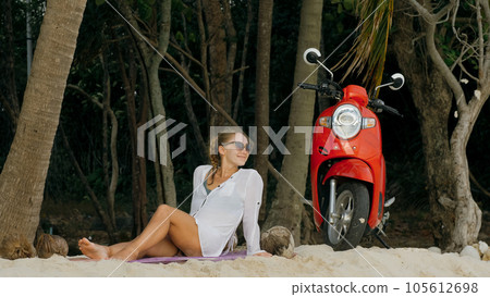 Scooter road trip. Woman alone on red motorbike in white clothes on sand beach by ocean. One girl caucasian tourist walk near tropical palm tree. 105612698