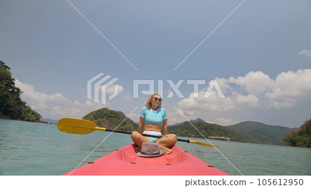 Sportive woman rows pink plastic canoe along sea water. Positive sports girl hand padding on kayak, front view. 105612950