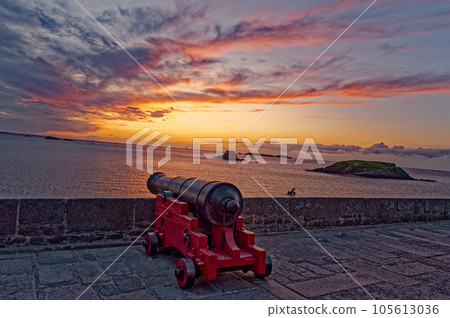 Ancient weapons on the fortress against the backdrop of the ocean and orange sky Ancient weapons on the fortress against the backdrop of the ocean and orange sky 105613036