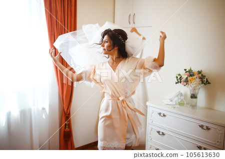 Elegant bride in white robe posing under curtain. Amazing bride in the morning preparation. Elegant bride in white robe posing under curtain. Amazing bride in the morning preparation. 105613630