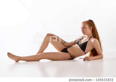 Relaxed young girl with fit, slim figure lying on floor, posing in underwear against white studio background 105615853