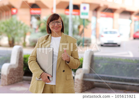 Confident motivated adult businesswoman start own startup remote, hold laptop smiling broadly, shows thumb up, like advert, recommends good co-working space, stand outdoors. Business concept 105615921
