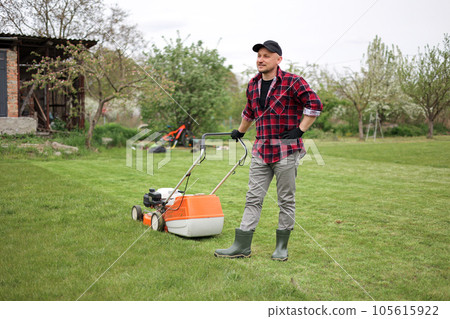 man makes a short break while cutting grass with a lawn mower after at backyard of his house. Gardening, sweating or exhausted male resting after working outdoor household chores 105615922