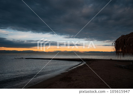 Romantic landscape - Sunrise, soft orange sky, illuminated mountains, sea, beach, pier and beach lounger with an umbrella. The concept of a date and a meeting of the sunrise at the sea. Romantic landscape - Sunrise, soft orange sky, illuminated mountains, sea, beach, pier and beach lounger with an umbrella. The concept of a date and a meeting of the sunrise at the sea. 105615947