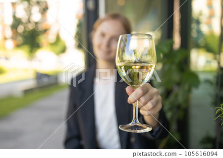 Woman drinking white wine from a glass at city cafe. Beautiful female enjoying cozy evening on terrace. Summertime relax at sunny patio. Woman drinking white wine from a glass at city cafe. Beautiful female enjoying cozy evening on terrace. Summertime relax at sunny patio. 105616094