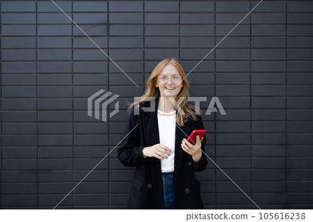 Cheerful blonde business woman standing isolated over gray wall background, holding mobile phone. Smiling lovely young woman standing and using cell phone over grey background Cheerful blonde business woman standing isolated over gray wall background, holding mobile phone. Smiling lovely young woman standing and using cell phone over grey background 105616238