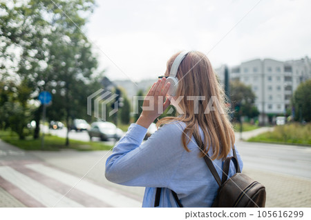 Back view of young blonde Caucasian woman listening the music waiting at traffic lights to cross street Back view of young blonde Caucasian woman listening the music waiting at traffic lights to cross street 105616299