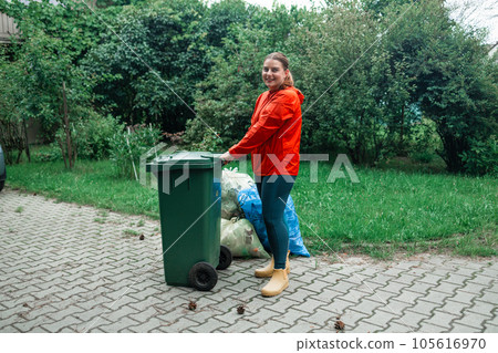 Adult woman household taking out bin to the street on rubbish day. 105616970
