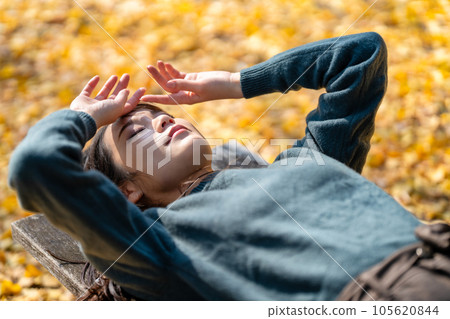 A woman lying on a bench in autumn leaves 105620844