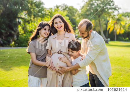 A loving family enjoying a leisurely walk in the park - a radiant pregnant woman after 40, embraced by her husband, and accompanied by their adult teenage children, savoring precious moments together 105621614