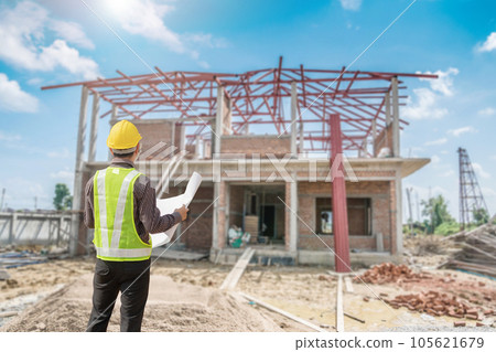 young professional engineer in protective helmet and blueprints paper at the house building construction site 105621679