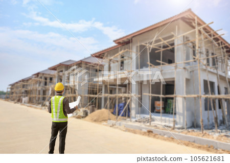 young professional engineer in protective helmet and blueprints paper at the house building construction site 105621681