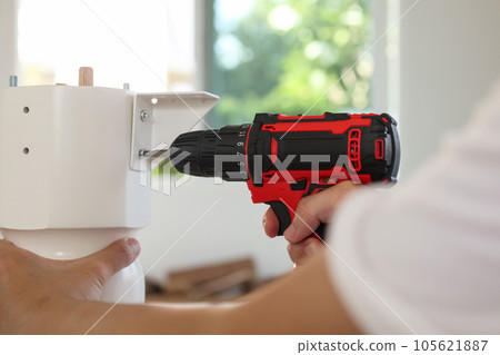 man assembling white table furniture at home using cordless screwdriver man assembling white table furniture at home using cordless screwdriver 105621887