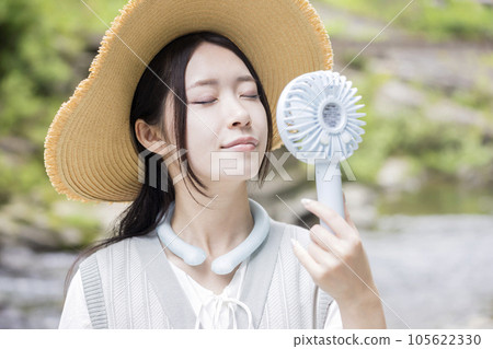 一位戴著草帽的年輕女子在河邊使用帶有頸部冷卻器的便攜式風扇 一位戴著草帽的年輕女子在河邊使用帶有頸部冷卻器的便攜式風扇 105622330
