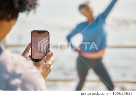 Phone, fitness and photograph of woman at beach in silly pose at sea for senior friends. Exercise, mobile and picture for social media post on a ocean promenade walk for nature workout and friendship Phone, fitness and photograph of woman at beach in silly pose at sea for senior friends. Exercise, mobile and picture for social media post on a ocean promenade walk for nature workout and friendship 105625625