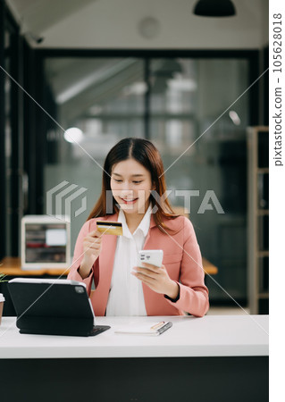 Asian Woman using smart phone for mobile payments online shopping,omni channel,sitting on table,virtual icons graphics interface screen 105628018