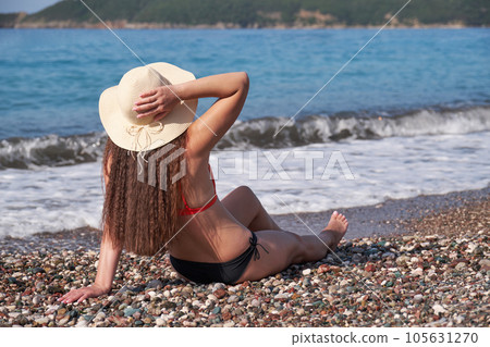 A beautiful woman in a hat enjoys the sun and sea breeze on the beach. 105631270