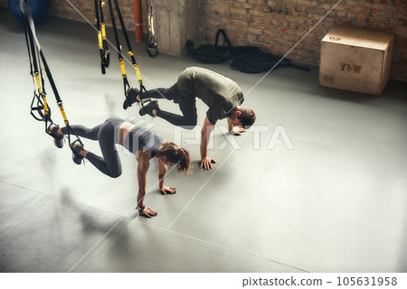 Young and sporty. Top view of a couple in sportswear training with Trx fitness straps at gym 105631958