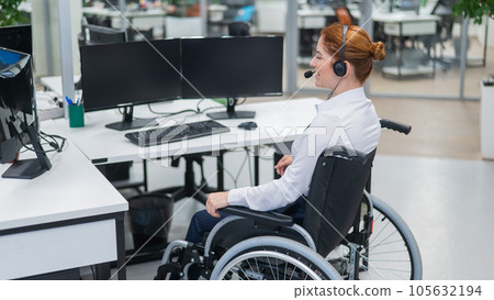 Red-haired caucasian woman in a wheelchair talking on a headset. Female call center worker at her desk. Red-haired caucasian woman in a wheelchair talking on a headset. Female call center worker at her desk. 105632194