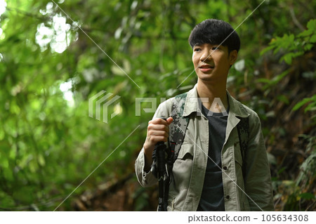 Happy male hiker with backpack and trekking sticks trekking in forest, exploring nature. Travel, adventure and active life concept. 105634308