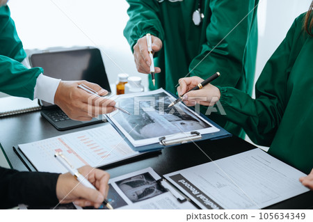 Medical team having a meeting with doctors in white lab coats and surgical scrubs seated at a table discussing a patients working online using computers in the medical industry. Medical team having a meeting with doctors in white lab coats and surgical scrubs seated at a table discussing a patients working online using computers in the medical industry. 105634349