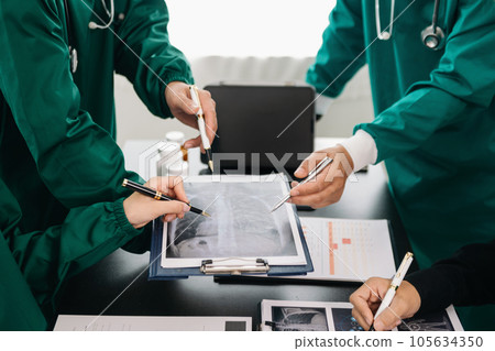 Medical team having a meeting with doctors in white lab coats and surgical scrubs seated at a table discussing a patients working online using computers in the medical industry. 105634350