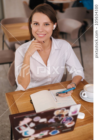 Young business lady work in cafe. Female using wireless headphones, smartphone, laptop and notebook. Freelancer concept Young business lady work in cafe. Female using wireless headphones, smartphone, laptop and notebook. Freelancer concept 105634380