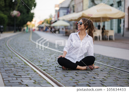 Woman in formal outfit and sunglasses sitting on street in centre of city 105634433