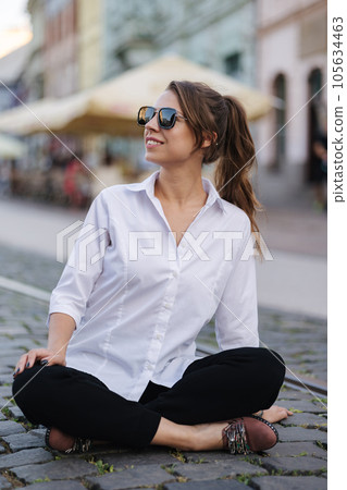Woman in formal outfit and sunglasses sitting on street in centre of city Woman in formal outfit and sunglasses sitting on street in centre of city 105634463