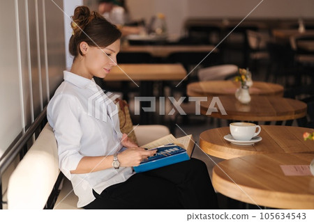 Side view of woman reading book in cafe 105634543