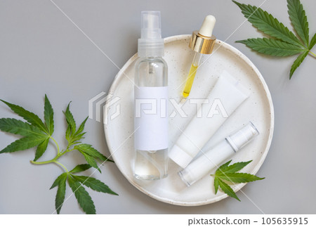 Cosmetic bottles with blank label and pipette near green cannabis leaves on grey. Mockup Cosmetic bottles with blank label and pipette near green cannabis leaves on grey. Mockup 105635915