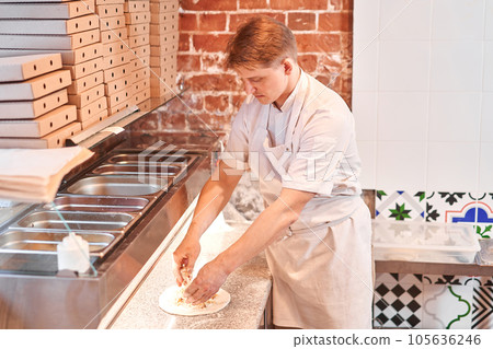 Raw pizza ready to bake. The chef prepares pizza. boxes for food delivery on background. Neapolitan pizza from a wood-fired oven. Raw pizza ready to bake. The chef prepares pizza. boxes for food delivery on background. Neapolitan pizza from a wood-fired oven. 105636246
