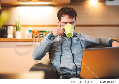 Waist up caucasian man sitting on the couch having a cup of coffee while listening to online classes on his laptop  105636428