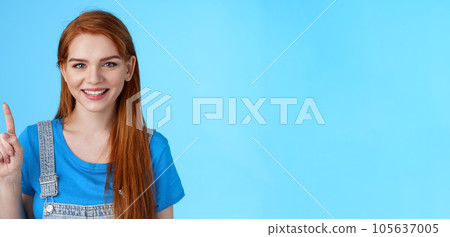 Close-up cute tender redhead european female make order, show number one first, smiling friendly carefree, extend finger, pointing up, counting stand blue background joyful 105637005