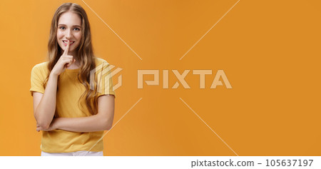 Girl wants keep secret betweet us. Portrait of charming good-looking slim pretty and young woman with long wavy hair and tattoo showing shh gesture with index finger over mouth against orange wall Girl wants keep secret betweet us. Portrait of charming good-looking slim pretty and young woman with long wavy hair and tattoo showing shh gesture with index finger over mouth against orange wall 105637197
