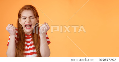 I did it. Charming lucky determined redhead female achieve success, fist pump celebrating, close eyes yell yes yeah, hooray gesture, triumphing victory, very good news, stand orange background 105637202