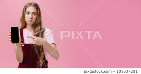 Sad gloomy young female with cute wavy natural hairstyle showing smartphone screen pointing at gadget with index finger making upset face frowning displeased feeling regret after buying broken phone Sad gloomy young female with cute wavy natural hairstyle showing smartphone screen pointing at gadget with index finger making upset face frowning displeased feeling regret after buying broken phone 105637281