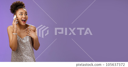 Impressed sociable african-american talkative woman in silver dress talking smartphone pointing herself amused describing emotions impressions after visit awesome party, blue background 105637372