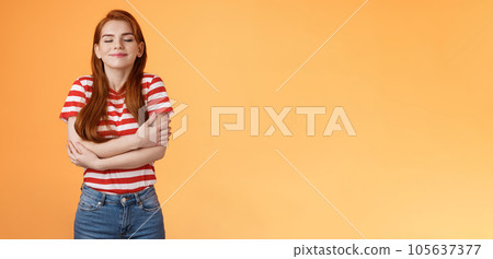 Tender lovely redhead modern woman embrace own body, feel happiness self-acceptance, smiling close eyes, cross arms, hugging herself dreamy, imaging something, daydreaming orange background 105637377