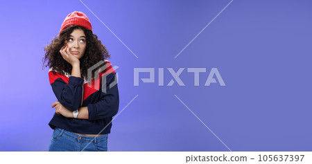 Portrait of frustrated and bored lonely girl with curly hair in winter hat holding hand across chest leaning head on palm, looking silly and gloomy at upper right corner, thinking feeling boredom 105637397
