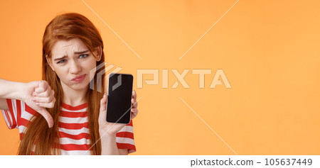 Very bad poor quality. Upset redhead female customer grimace disappointed, show smartphone blank display, thumbs down judgement, dislike app, smirk dismay, stand upset orange background Very bad poor quality. Upset redhead female customer grimace disappointed, show smartphone blank display, thumbs down judgement, dislike app, smirk dismay, stand upset orange background 105637449