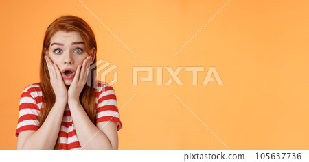 Close-up shocked speechless redhead woman, drop jaw gasping, touch cheeks embarrassed shook, look pity shame, stare camera astonished, surprised hear disturbing news, orange background 105637736