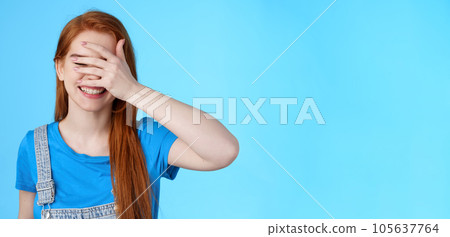 Cheerful tender redhead girlfriend feel happy, enjoy summer holiday, relaxing joyful weekend, playful mood, close eyes hold palm face, hide-n-seek pikaboo gesture, stand blue background 105637764