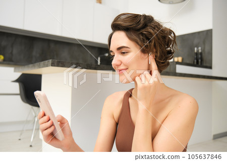 Close up of young fitness instructor, healthy and fit woman with smartphone, wireless headphones, records her workout training session at home, connects to client on video call for yoga classes 105637846